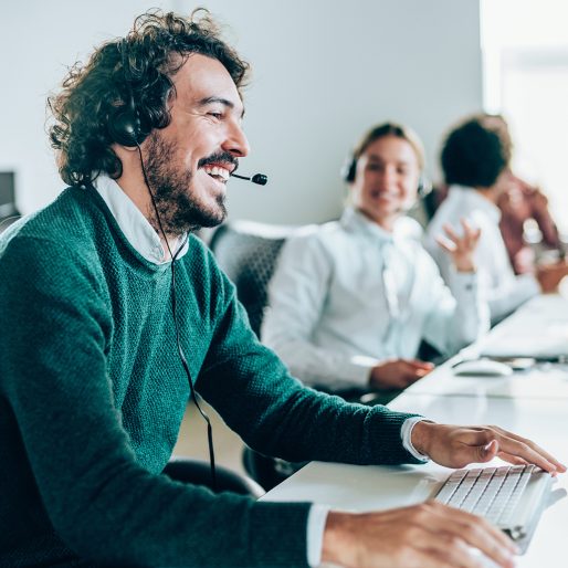 Smiling handsome young businessman working in call center. Shot of a cheerful young man working in a call center with his team. Confident male operator is working with colleagues. Call center operators sitting in a row at desks.