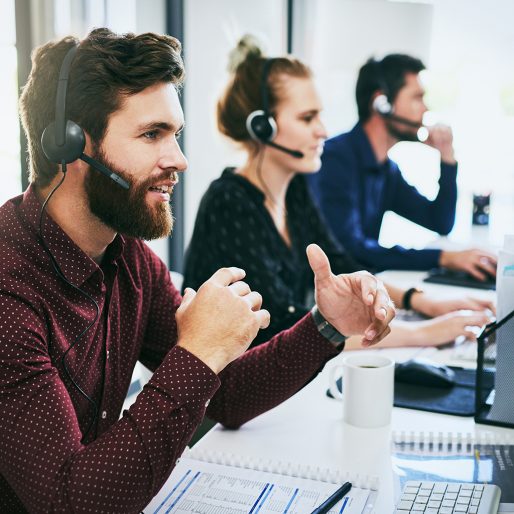 Cropped shot of a handsome young businessman wearing a headset and using a computer while sitting with his colleagues