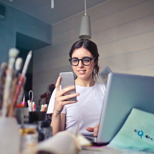 woman-in-white-t-shirt-holding-smartphone-in-front-of-laptop_1024x1024