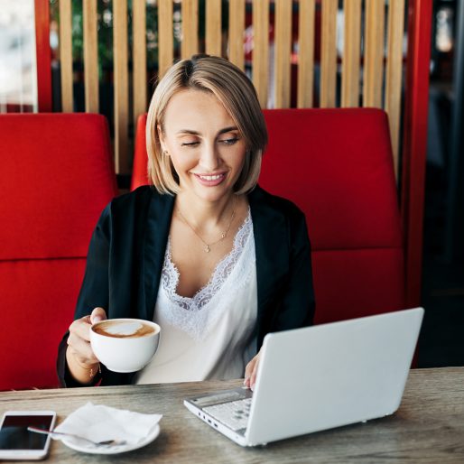 Portrait of a young woman drinking coffee and using a laptop in a cafe.